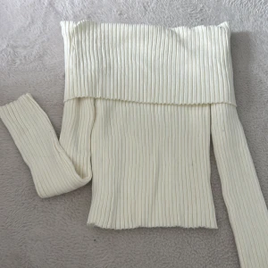 Offshoulder ribbad vit tröja - Trendig offshoulder tröja i ribbad, stretchig kvalitet. Färgen är krämvit och modellen är figurnära med långa ärmar. Perfekt för dig som gillar en stilren och modern look med lite edge. Köpt från Nelly.