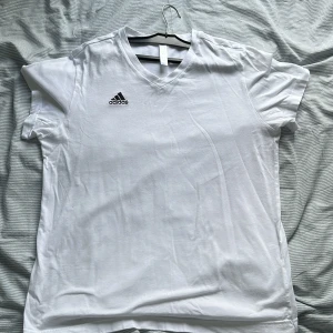 Vit Adidas t-shirt med v-ringning - Klassisk vit t-shirt från Adidas med v-ringad hals i storlek L med liten i storleken 
