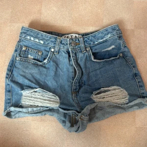 Blå jeansshorts med slitningar från Stay - Snygga blå jeansshorts från Stay i modell XS. Slitna detaljer framtill och uppvikta benslut. Klassisk femficksdesign och dragkedja med knapp. Perfekta för en chill sommarlook.