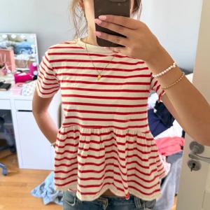 Randig rödvit tröja från Zara - Supersöt tröja från Zara i rödvitt randigt mönster. Modellen har kort ärm, rund hals och en volangig, lös passform nedtill som ger en flowy känsla. 