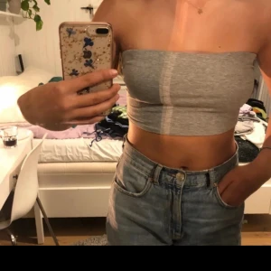 Grå bandeau tubtopp från Boohoo - Säljer en enkel och stilren grå bandeau tubtopp från Boohoo. Toppen är ärmlös och axelbandslös, perfekt till jeans eller kjol. Gjord i mjuk bomullsmix som sitter skönt och följsamt mot kroppen. Supersnygg till sommaren eller festival!