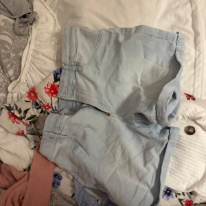 Ljusblåa denimshorts från H&M - Snygga ljusblåa shorts i jeansmaterial från H&M. Klassisk femficksmodell med dragkedja och knapp framtill. Perfekta för varma dagar och enkla att matcha med allt. Stilen är avslappnad och passar dig som gillar en clean look.