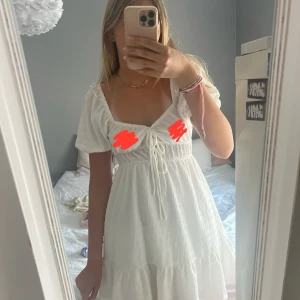 Vit kort klänning med snörning - Superfin vit kort klänning med puffärmar och söt snörning framtill. Klänningen har volang nertill och en lätt strukturerad bomullskänsla. Perfekt för varma dagar och har en romantisk vibe med sin omlottliknande byst och rynkade detaljer.