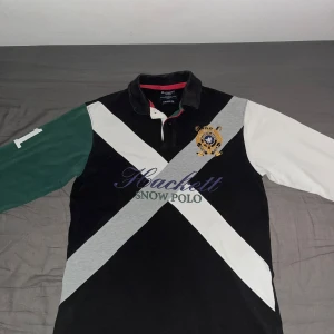 Hackett Snow Polo pikétröja S - Snygg långärmad pikétröja från Hackett London i svart, vitt, grått och grönt. Broderad logga och emblem på bröstet, klassisk krage och kontrastärmar. Tillverkad i bomull med skräddarsydd passform. Perfekt för dig som gillar sportig och preppy stil.