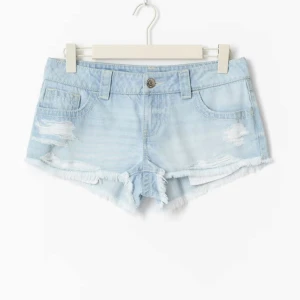 Slutsålda jeansshorts - (Dom är aldrig använda och prislappen är kvar) Snygga ljusblå jeansshorts med slitna detaljer och fransad kant. Klassisk femficksmodell med låg midja och dragkedja fram. Perfekta för varma dagar och ger en avslappnad vibe. Shortsen har bakfickor med dekorativa sömmar och är tillverkade i mjukt denimtyg.