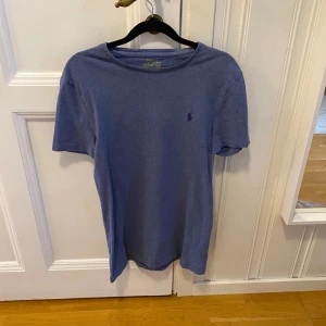 Blå t-shirt från Ralph Lauren - Snygg blå t-shirt från Ralph Lauren i en custom slim fit. Den har en broderad logga på bröstet och är tillverkad i mjukt material. Perfekt för en stilren och avslappnad look.