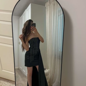 Svart axelbandslös klänning med släp - Unik svart klänning i egen design – sitter perfekt och framhäver kroppens symmetri på ett smickrande sätt. Endast använd en gång, i utmärkt skick. Finns i storlek S och XS. En riktig statement-piece som får dig att sticka ut och stråla vid varje tillfälle. Pris: 1400 kr.