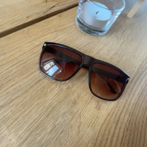 Bruna fyrkantiga solglasögon - Snygga solglasögon med breda, fyrkantiga bågar i mörkbrunt plastmaterial. Glasen är tonade i brunt och ger en cool retrovibe. Perfekta för att lyfta din stil under soliga dagar.