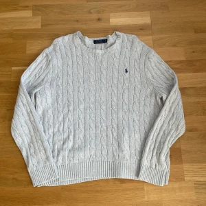 Ljusgrå Polo Ralph Lauren tröja - Kabelstickad ljusgrå tröja från Polo Ralph Lauren i nyskick, tröjan är knappt använd. Priset är ej hugget i sten