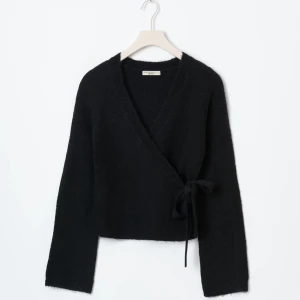 Svart omlottkofta - Mysig svart omlottkofta från Gina Tricot med knyt i sidan och v-ringad hals. Koftan är stickad och har långa ärmar med lite vidare avslut. Perfekt för lager-på-lager och ger en chill men ändå stilren vibe. Slutsåld på hemsidan och knappt använd därav priset😊