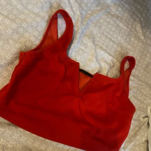 Röd croppad linnetopp med v-ringning - Snygg röd croppad linnetopp med breda axelband och en cool v-ringad detalj framtill. Perfekt för dig som vill sticka ut med en färgstark och trendig topp. Enkel att matcha med både jeans och kjol.