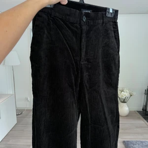 Svarta manchesterbyxor - Svarta manchesterbyxor från Lindex i klassisk rak modell. Byxorna har normal passform, hällor för bälte, knapp och dragkedja framtill samt fickor både fram och bak. Perfekta för dig som gillar en stilren och tidlös look. Använda max 5 gånger. Önskar du veta exakta mått? Tveka inte att höra av dig!