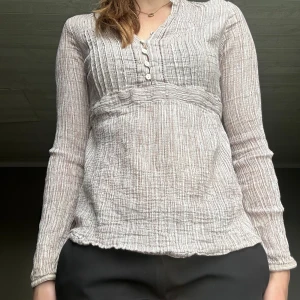Randig blus med knappar från Lindex - Superfin blus från Lindex i ljusbeige och vit med tunna ränder. Blusen har v-ringning, små knappar framtill och snörning i ryggen för snygg passform. Långärmad och tillverkad i ett mjukt, strukturerat bomullstyg. Perfekt för en chill och stilren look. En trasig knapp högst upp😊passar mig som brukar ha S 