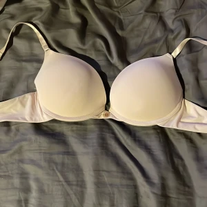 Ljusbeige push up bh - Säljer en ljusbeige bh med vadderade kupor. Bh:n har en liten rosett mellan kuporna och släta, mjuka material. Perfekt under toppar med bara axlar eller tunnare plagg.