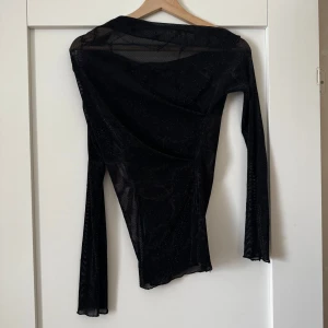 Svart mesh topp med glitter - Säljer en svart mesh topp med glittrigt tyg och lång ärm. Tunt och genomskinligt material som ger en cool och trendig look. Perfekt att styla lager på lager eller till festligare tillfällen.