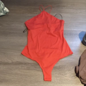 Röd body från H&M - En enkel och stilren röd baddräkt från H&M med tunna axelband. Perfekt för strand eller pool och har en klassisk passform. Materialet känns mjukt och stretchigt för en bekväm känsla.