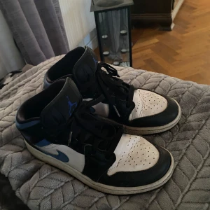 Nike Air Jordans svart/vit/blå - Säljer ett par Nike Air Jordans i svart, vitt och blått. Skorna har hög modell med snörning och rund tå. Väl använda men inget fel på dom förutom att det börjar bli ett litet hål på vänster häl💕