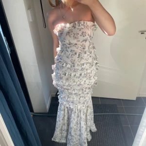 Vit blommig långklänning med volanger - Superfin axelbandslös långklänning i vitt med blommigt mönster och volanger över hela klänningen. Klänningen är mycket sommrig och perfekt till varma sommarkvällarperfekt och speciella tillfällen, aldrig använt🤍🌼☀️