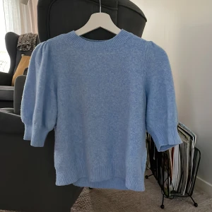 Ljusblå stickad tröja från Vero Moda - Superfin ljusblå stickad tröja från Vero Moda med kortare ärmar och ribbade muddar. Perfekt för dig som vill ha en mjuk och stilren tröja med lite puff vid axlarna. Snygg till både jeans och kjol!