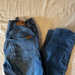 Blå jeans från Name It - Säljer ett par klassiska blå jeans från Name It med normal passform. Jeansen har fem fickor, dragkedja och knapp framtill samt snygga kontrastsömmar. Perfekta till vardags och lätta att matcha med olika stilar.