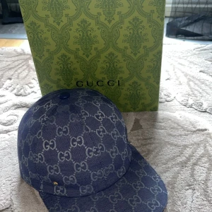 Blå keps från Gucci med monogram - Säljer en blå keps från Gucci med klassiskt GG-monogram i ljusare blått. Kepsen har böjd skärm och är tillverkad i ett tygmaterial med vit insida. Perfekt för dig som gillar exklusiva accessoarer. Den är äkta min mamma tappa bort kvitto så jag släpper den lite biligare aldrig använd.