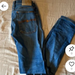 Blå jeans från Nudie Jeans - Säljer ett par klassiska blå jeans från Nudie Jeans med raka ben och normal passform. Jeansen har fem fickor, orangea sömmar och knappgylf. Perfekta för dig som gillar stilrena och tidlösa jeans. Kan ge mer bilder och sänka priset 