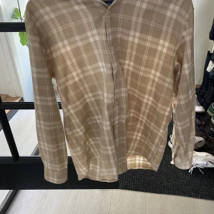 Beige rutig skjorta från Pull&Bear - Säljer en beige och vit rutig skjorta från Pull&Bear i relaxed fit. Skjortan har långa ärmar och knäppning framtill. Perfekt för en avslappnad och stilren look.