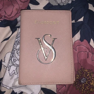 Rosa passfodral från Victoria's Secret - Säljer ett snyggt rosa passfodral från Victoria's Secret med guldiga detaljer och VS-logga framtill. Insidan har ett coolt leopardmönster och plats för passet. Perfekt accessoar för resan!