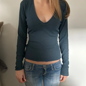 Mörkblå ribbad topp - Säljer en snygg mörkblå ribbad topp med v-ringning och långa ärmar. Toppen har en knytning i ryggen som ger en fin detalj. Perfekt för en stilren look.