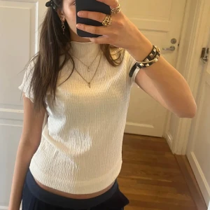Vit ribbad topp med kort ärm - Säljer en vit ribbad topp med korta ärmar och hög hals. Toppen har en lätt croppad passform och är perfekt för en stilren look. Enkel att matcha med både jeans och kjol.