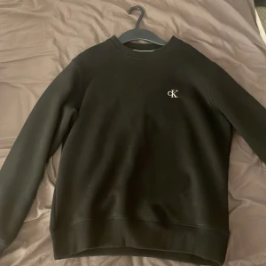 Svart sweatshirt från Calvin Klein Jeans - Säljer en svart sweatshirt från Calvin Klein Jeans med CK-logga på bröstet och broderad text på ärmen. Använd Max 5 gånger