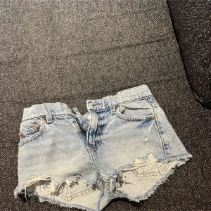 Ljusblå jeansshorts med fransar från Gina Tricot - Säljer ett par ljusblå jeansshorts från Gina Tricot med råa fransade kanter och klassisk femficksdesign. Shortsen har bälteshällor och knappgylf, perfekt för sommardagar.