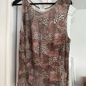 Mönstrad ärmlös linnetopp från Trofé - Säljer en ärmlös linnetopp från Trofé med djurmönster i bruna och beige toner. Toppen har rund halsringning och är tillverkad i ett mjukt material, perfekt för varma dagar. Strl L