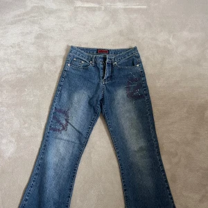 Blå bootcut jeans med lågmidja frånWei Niu - Säljer ett par blå bootcut lowrise jeans från Wei Niu med snygga detaljer på fram- och baksidan. Jeansen har en liten defekt på baksidan och saknar knapp men är annars i bra skick!🥰💕