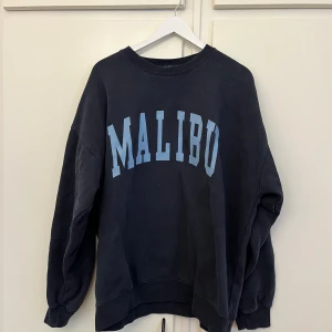 Tröja  - Säljer en mörkblå sweatshirt från Brandy Melville med  ljusblått 'Malibu'-tryck på framsidan i storlek onesize. Använd ett fåtal gånger men bra skick!! 🙌🏽