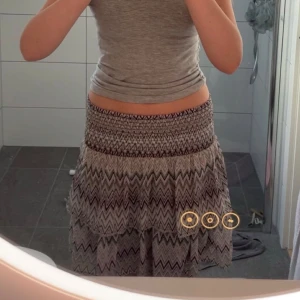 Grå mönstrad kjol med volang - Supersöt mönstrad kjol med svart sicksackmönster, lila, turkos, grön och volang. Resår i midjan gör den bekväm och lätt att bära. Perfekt till varma dagar och enkel att matcha med olika toppar.