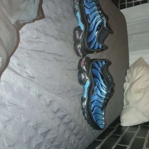 Nike Air Max Plus TN blå och svarta sneakers - Säljer ett par Nike Air Max Plus TN sneakers i blått och svart med svarta detaljer och synlig luftdämpning i sulan. Skorna har snörning och en vågig design på ovandelen. Perfekta för dig som gillar streetwear och sportig stil.