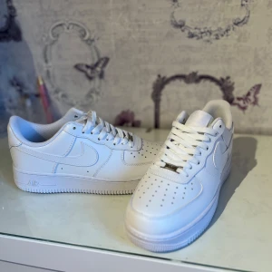 Nike Air Force 1 vita sneakers - Klassiska vita Nike Air Force 1 sneakers med låg profil och rund tå. Skorna har snörning och är tillverkade i skinn med perforerade detaljer framtill för extra ventilation. Perfekta för en stilren och tidlös look.  Helt nya aldrig använda säljer för de var för stora då de är lite stora i storleken för mig men nu pris är 1499kr