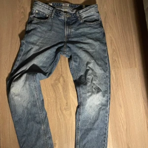 Jack & Jones jeans, knappt använda  - Säljer ett par klassiska blå jeansbyxor med raka ben och fem fickor. Byxorna har normal passform och stängs med dragkedja och knapp. Perfekta för en avslappnad stil.