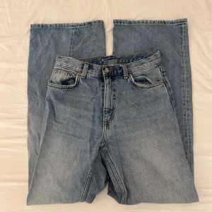 Blå vida jeans från Monki - Säljer ett par snygga blå jeans från Monki i strl 26 med vida ben. Jeansen har fem fickor, bälteshällor och stängs med dragkedja och knapp. Tillverkade i 100% bomull. 