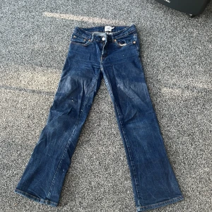 Blå bootcut jeans från 157 - Ett par klassiska blå bootcut jeans från 157 med snygga bakfickor med lock och knappar. Jeansen har normal passform och är i modellen short. Perfekta för dig som gillar en tidlös denimlook.