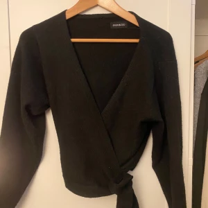 Svart omlottkofta från Even&Odd - Säljer en svart omlottkofta från Even&Odd med knyt i midjan. Tröjan har lång ärm och djup v-ringning. Perfekt att styla med jeans eller kjol. Mjuk och skön att bära.