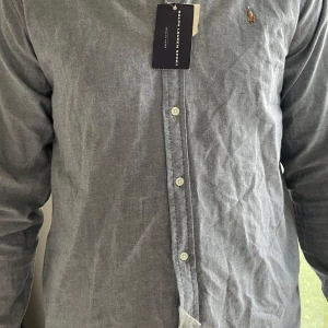 Ljusblå skjorta från Ralph Lauren - Säljer en stilren ljusblå skjorta från Ralph Lauren med klassisk broderad logga på bröstet. Skjortan är i slim fit-modell, har långa ärmar och knäppning framtill. Tillverkad i 100% bomull för en skön känsla. Priset är ej hugget i sten!