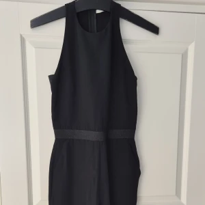 Svart onepiece med resårdetaljer - Säljer en svart onepiece med ärmlös design och breda resårdetaljer i midjan och på ryggen. Den har en stilren och minimalistisk look med öppen rygg och rund halsringning. Perfekt för dig som gillar enkel men snygg stil. Känns mer som stl 36 än 38