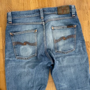 Blå jeans från Nudie Jeans Co - Säljer ett par klassiska blå jeans från Nudie Jeans Co med snygga slitningar och kontrastsömmar. Nypris ligger på ca 1700. 