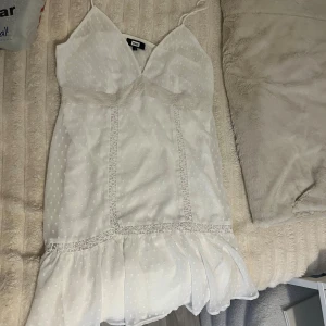 Vit prickig klänning från Bikbok - Söt vit klänning från Bikbok med tunna axelband och v-ringad hals. Klänningen har diskret prickigt mönster, spetsdetaljer och volang nertill. Perfekt för sommarens alla tillfällen!