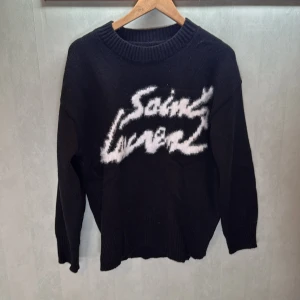 Svart stickad tröja från Saint Laurent - Svart stickad tröja med Saint Laurent-logga i vitt framtill. Tröjan har rund halsringning och långa ärmar med ribbade muddar. Perfekt för dig som vill ha en stilren look. Använd några fåtal gånger.