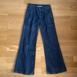 Blå wide leg jeans från Fascinate - Blå jeans från Fascinate med vida ben. De har dubbla knappar framtill, fina bakfickor med lock och knapp. De har pressveck och blir därför lite lika kostymbyxor. Ca 35 cm rakt över midjan och 77 i innerbenslängd.
