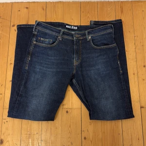 Mörkblå jeans från MAC Jeans - Säljer ett par klassiska mörkblå jeans från MAC Jeans med snygga kontrastsömmar och femficksdesign. Jeansen har normal passform och är tillverkade i ett slitstarkt denimtyg. Perfekta för dig som gillar stilrena och tidlösa byxor.