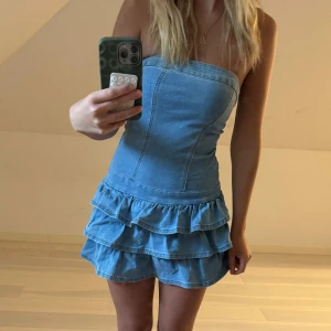 Jeansklänning med volang - Säljer en snygg axelbandslös jeansklänning med figurnära passform och dubbla volanglager nertill. Från shein därav pris